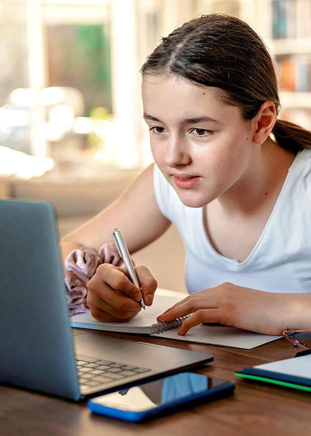 Student writing while looking at a laptop, portrait crop
